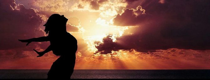 Silueta de una persona estirándose en la orilla del mar al atardecer.