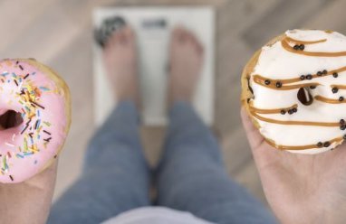 Persona de pie sobre una báscula digital sosteniendo dos donuts glaseados