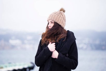 Mujer abrigada con gorro de lana mirando hacia el mar en un día frío