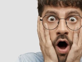Hombre con barba y gafas lleva las manos a la cara, sorprendido