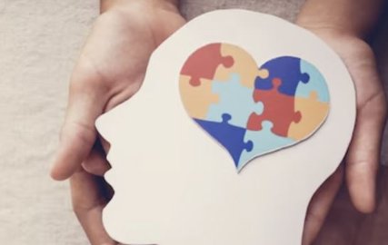 Manos sosteniendo una silueta de cabeza de papel con un corazón de piezas de puzle